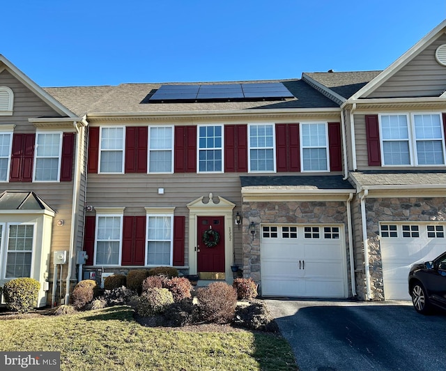 multi unit property featuring a garage, driveway, stone siding, and solar panels