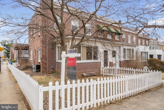 multi unit property featuring a fenced front yard, brick siding, central AC unit, and a chimney