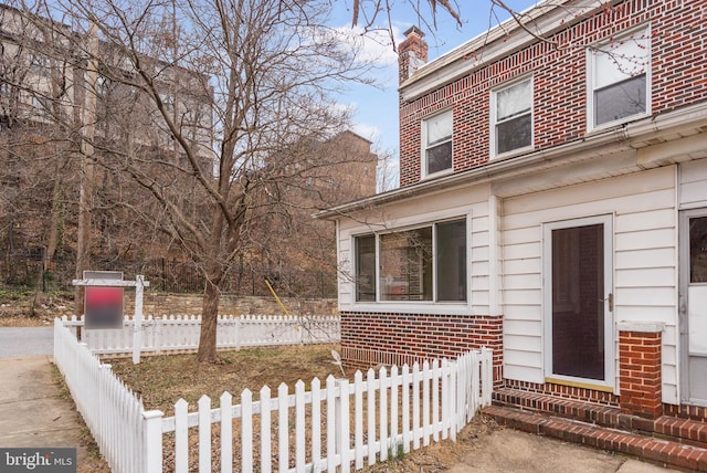 exterior space with brick siding, a chimney, and fence