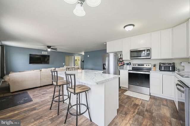 kitchen featuring a center island, dark wood finished floors, stainless steel appliances, white cabinetry, and a kitchen bar