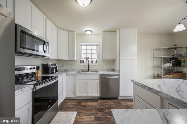 kitchen with white cabinets, light stone counters, dark wood-type flooring, stainless steel appliances, and a sink