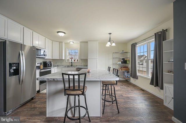 kitchen featuring white cabinets, dark wood-style floors, a breakfast bar area, a center island, and stainless steel appliances