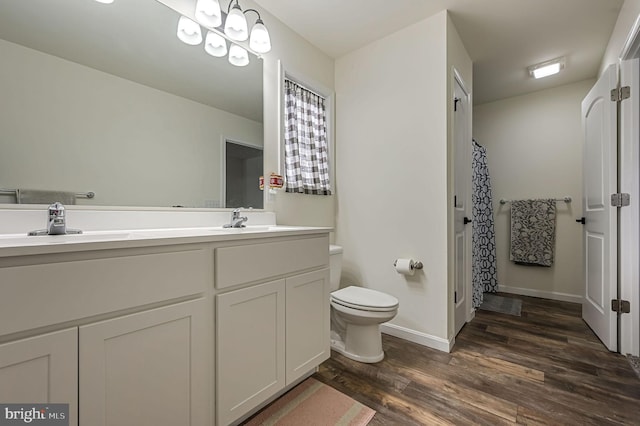 bathroom with double vanity, toilet, a sink, wood finished floors, and baseboards