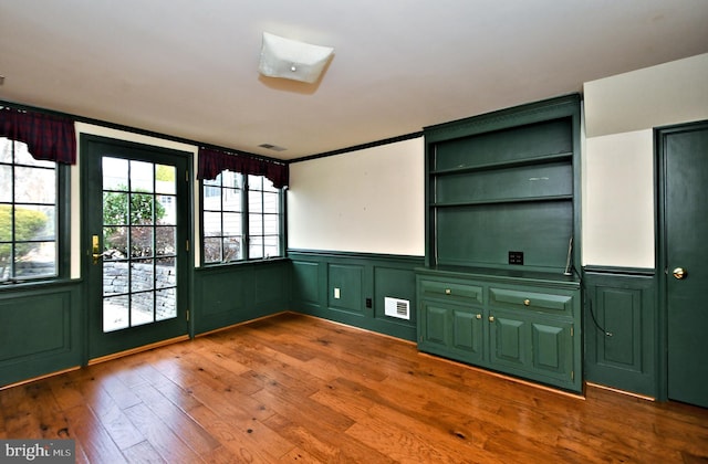 interior space with a wainscoted wall, visible vents, a decorative wall, and hardwood / wood-style flooring