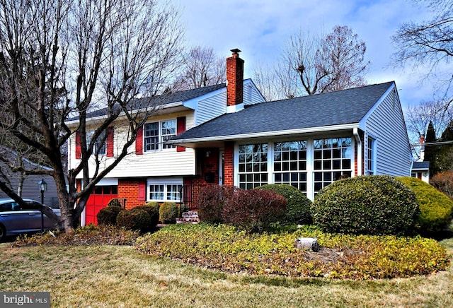 tri-level home with a shingled roof, brick siding, a chimney, and a front lawn