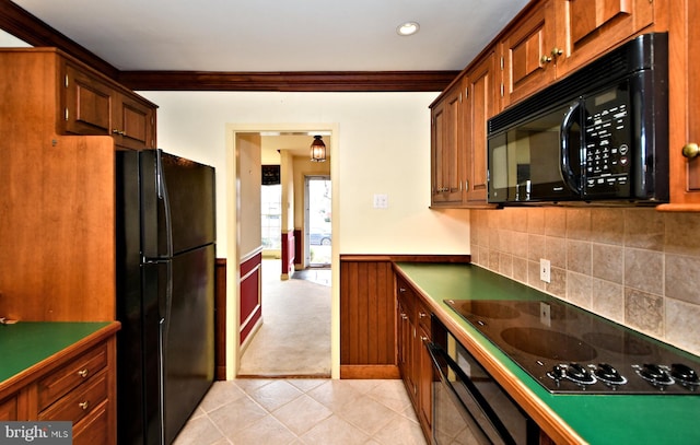 kitchen with wainscoting, crown molding, black appliances, backsplash, and light tile patterned flooring