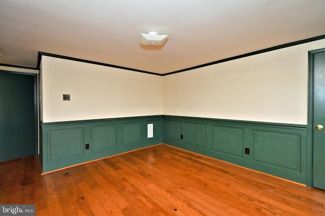 spare room with crown molding, wood finished floors, and wainscoting