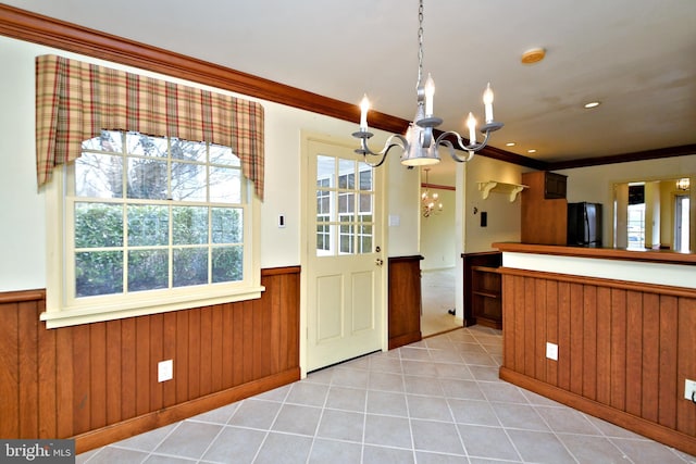 kitchen with light tile patterned flooring, a notable chandelier, a wainscoted wall, fridge, and crown molding