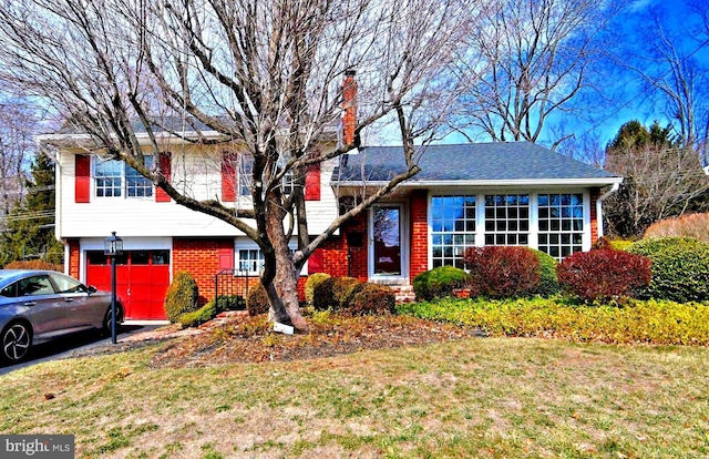 tri-level home with a garage, a front yard, brick siding, and a chimney