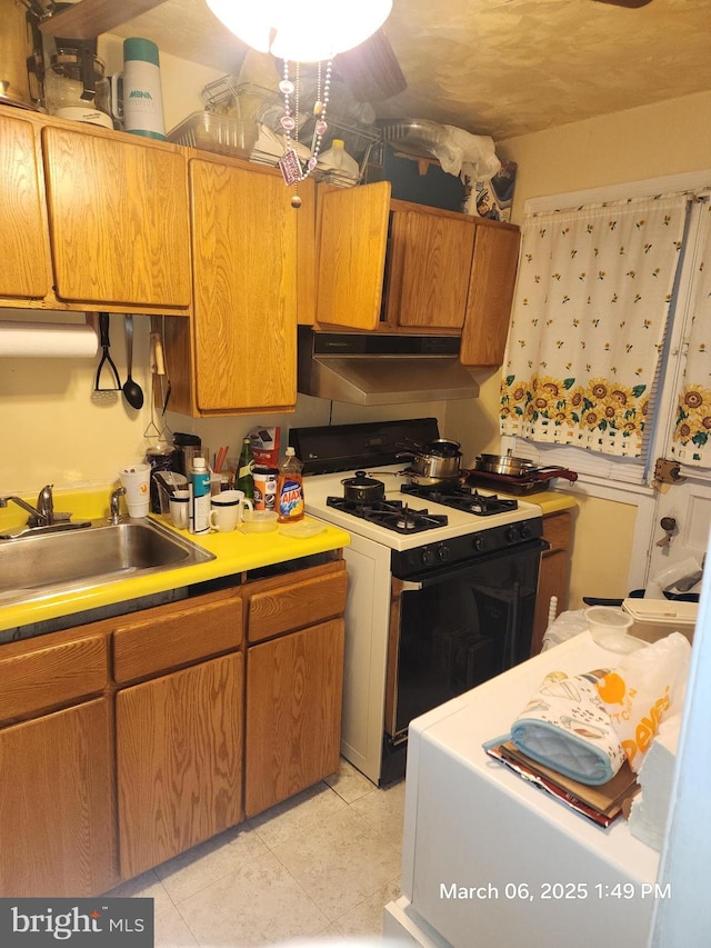 kitchen with gas stove, light countertops, under cabinet range hood, a sink, and light tile patterned flooring