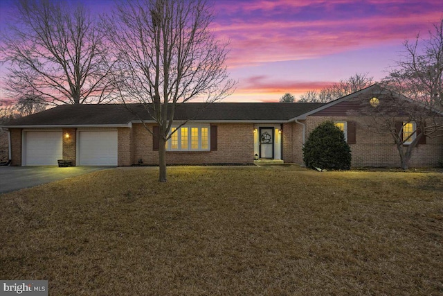 ranch-style home with driveway, brick siding, a lawn, and an attached garage