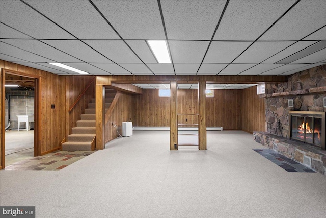 basement featuring wood walls, stairway, a drop ceiling, and a stone fireplace