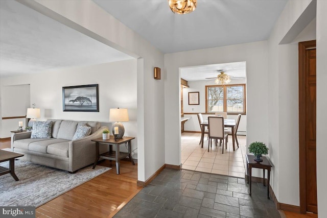 living area featuring stone tile floors, a ceiling fan, and baseboards