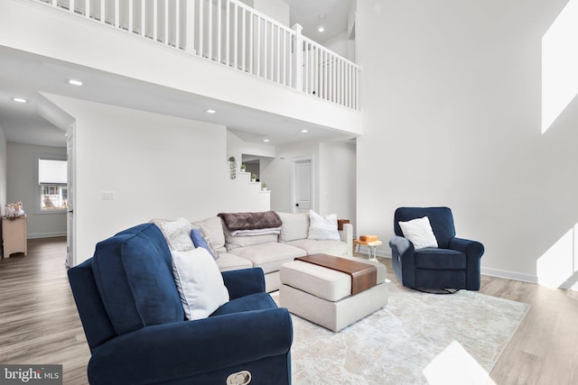 living area featuring recessed lighting, a towering ceiling, wood finished floors, baseboards, and stairs