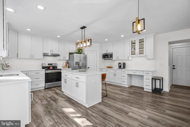 kitchen with white cabinets, dark wood-style floors, appliances with stainless steel finishes, under cabinet range hood, and a sink