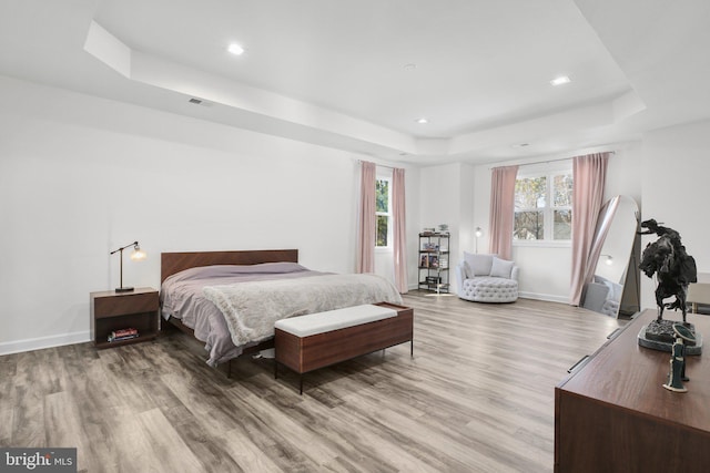 bedroom featuring wood finished floors, a raised ceiling, visible vents, and baseboards