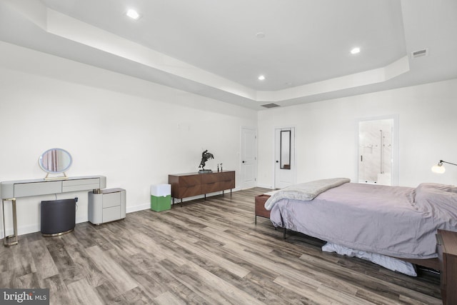 bedroom featuring a tray ceiling, visible vents, baseboards, and wood finished floors