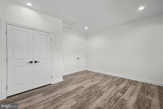 unfurnished bedroom with recessed lighting, wood finished floors, baseboards, a closet, and attic access