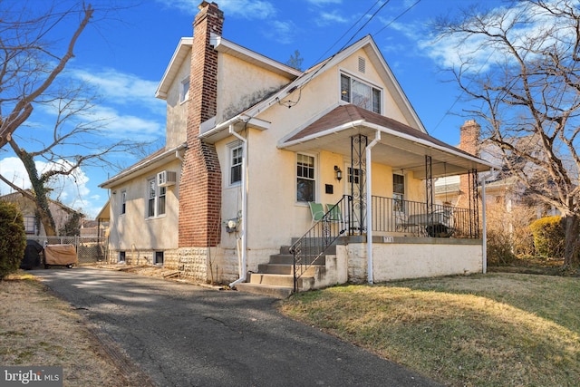 view of front of property featuring a wall mounted air conditioner, stucco siding, a porch, a front yard, and a chimney