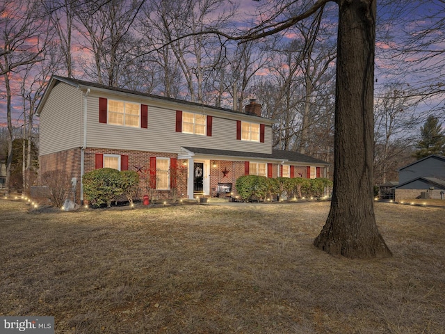 colonial home featuring a yard, brick siding, and a chimney