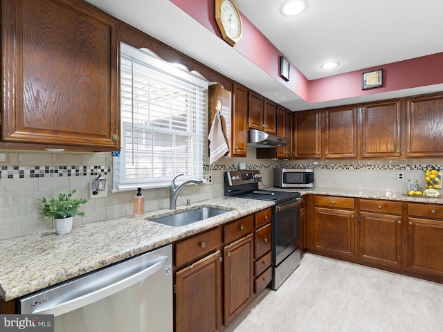 kitchen featuring decorative backsplash, light stone counters, appliances with stainless steel finishes, under cabinet range hood, and a sink