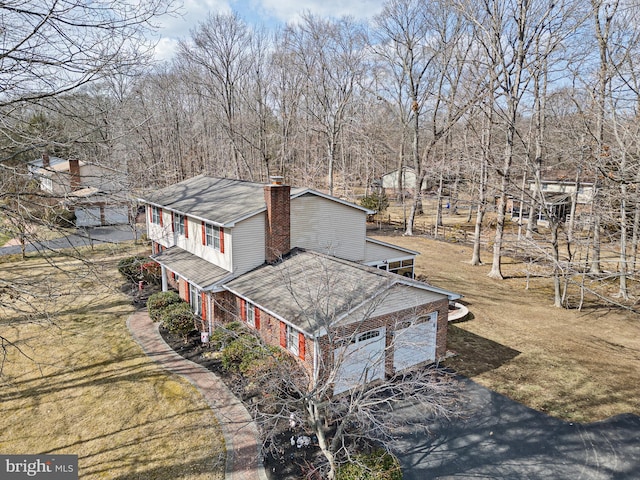 view of property exterior featuring a lawn, a chimney, aphalt driveway, an attached garage, and brick siding