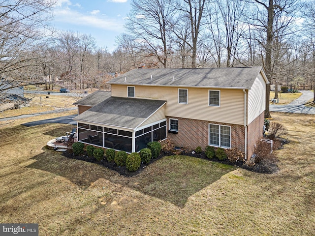 rear view of property featuring a sunroom, brick siding, a lawn, and a chimney