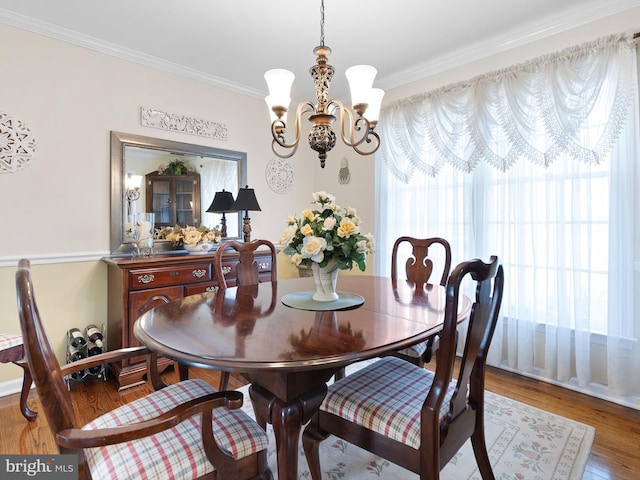 dining space with a chandelier, ornamental molding, and wood finished floors