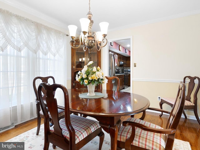 dining space with an inviting chandelier, crown molding, baseboards, and wood finished floors