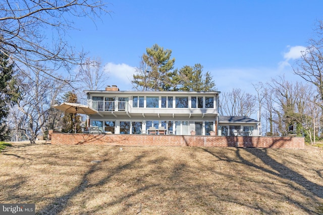 rear view of property featuring a chimney, a lawn, and a balcony