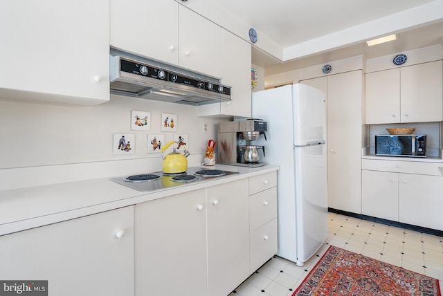 kitchen with under cabinet range hood, white cabinets, light countertops, freestanding refrigerator, and cooktop