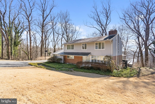 exterior space featuring driveway, brick siding, and a chimney