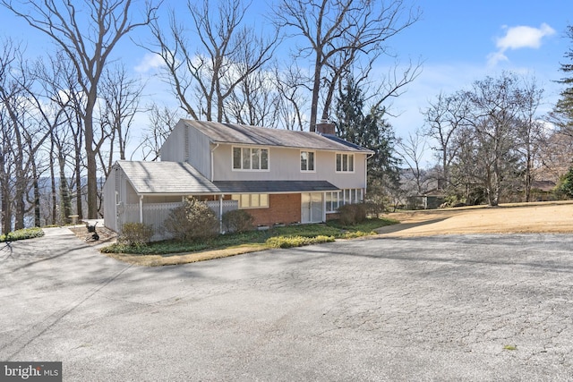 view of front of property with driveway, brick siding, and a chimney