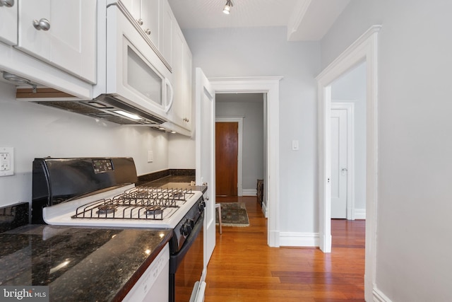 kitchen with gas range oven, light wood-style flooring, white microwave, white cabinets, and baseboards