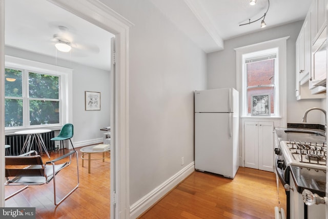 kitchen with light wood-type flooring, gas stove, a sink, and freestanding refrigerator