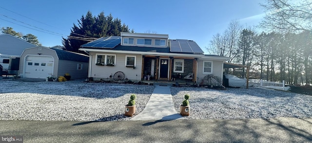 bungalow-style home featuring roof mounted solar panels, covered porch, driveway, and an outdoor structure