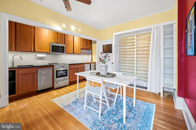 kitchen featuring light wood finished floors, stainless steel appliances, decorative backsplash, brown cabinetry, and a sink