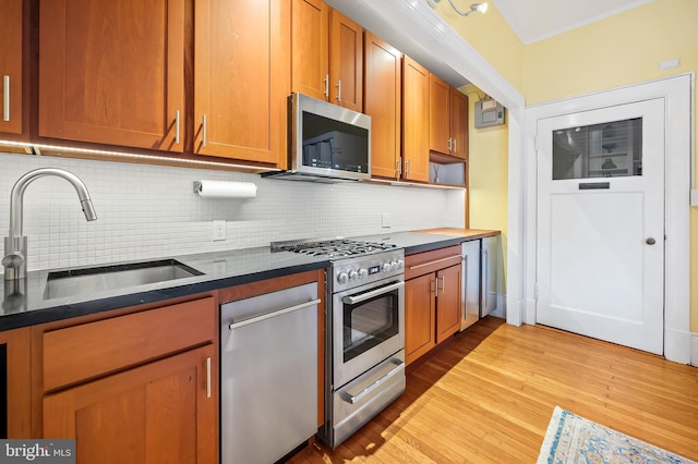 kitchen with brown cabinets, stainless steel appliances, decorative backsplash, a sink, and wood finished floors