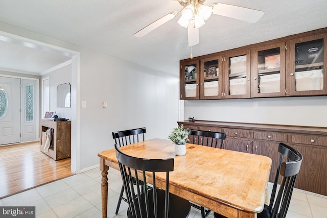 dining area with light tile patterned floors, ornamental molding, a ceiling fan, a textured ceiling, and baseboards