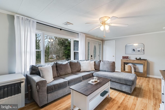 living room with ornamental molding, light wood-style flooring, visible vents, and baseboards