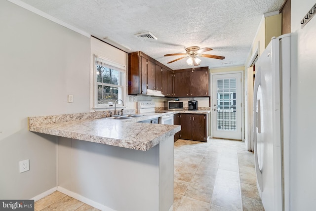 kitchen featuring visible vents, a sink, dark brown cabinetry, white appliances, and a peninsula