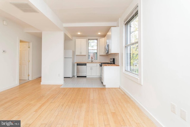 kitchen with stainless steel appliances, tasteful backsplash, visible vents, white cabinetry, and light wood-type flooring