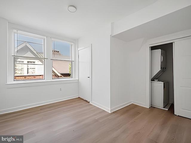 empty room with stacked washer / drying machine, baseboards, and wood finished floors