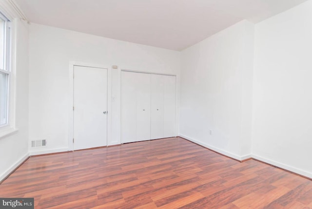 unfurnished bedroom with baseboards, multiple windows, visible vents, and wood finished floors