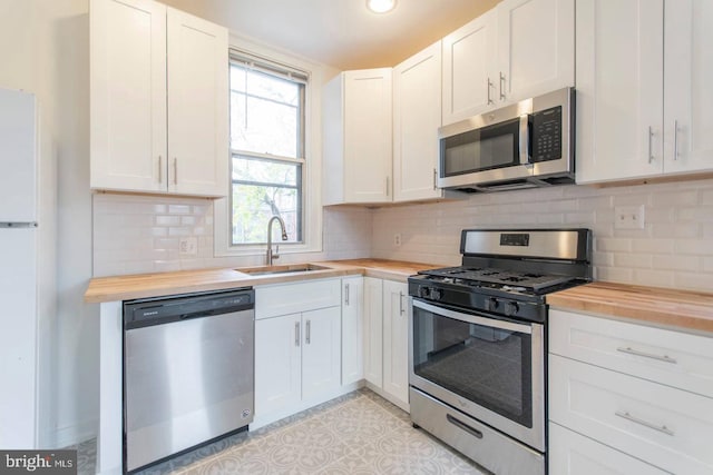 kitchen with stainless steel appliances, butcher block countertops, a sink, and white cabinetry