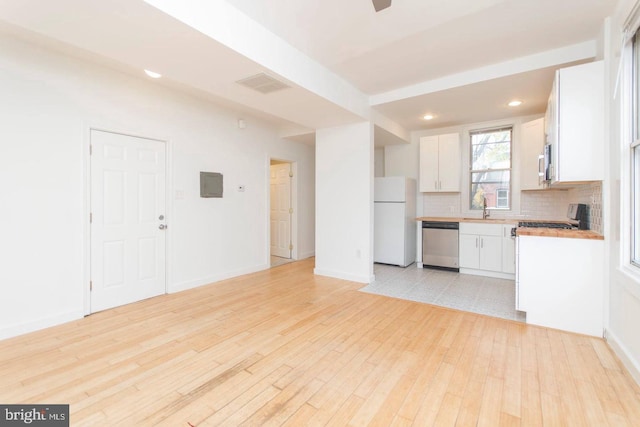 kitchen with stainless steel appliances, light countertops, backsplash, a sink, and light wood-type flooring