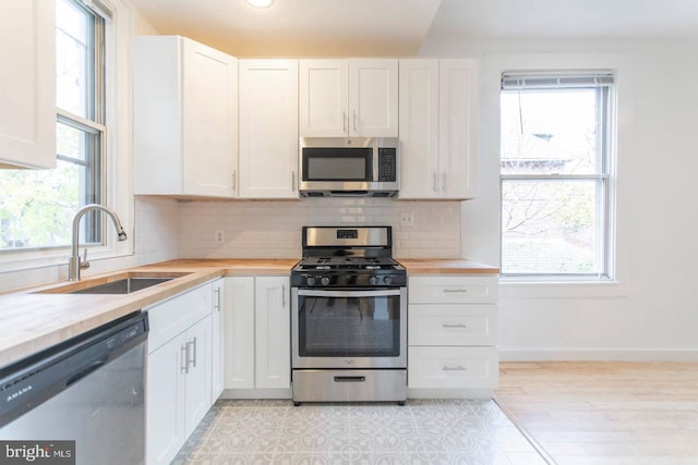 kitchen with a sink, baseboards, white cabinets, appliances with stainless steel finishes, and tasteful backsplash