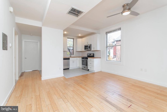 interior space featuring baseboards, visible vents, ceiling fan, light wood-type flooring, and a sink