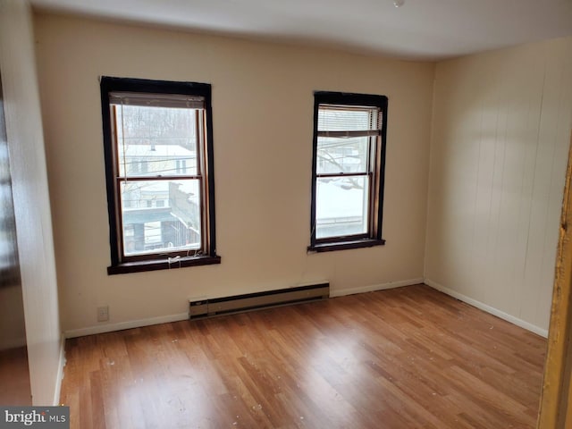 empty room featuring baseboards, a baseboard heating unit, and wood finished floors