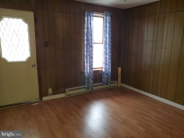 unfurnished room featuring baseboards, wooden walls, baseboard heating, and wood finished floors